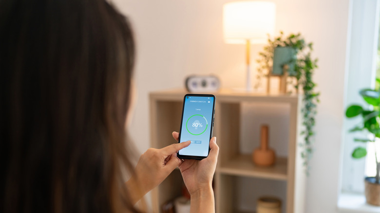 A person using their phone to control a smart table light in the background