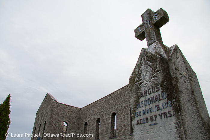 gravestone with roofless stone church in background at st. raphael's ruins in williamstown ontario