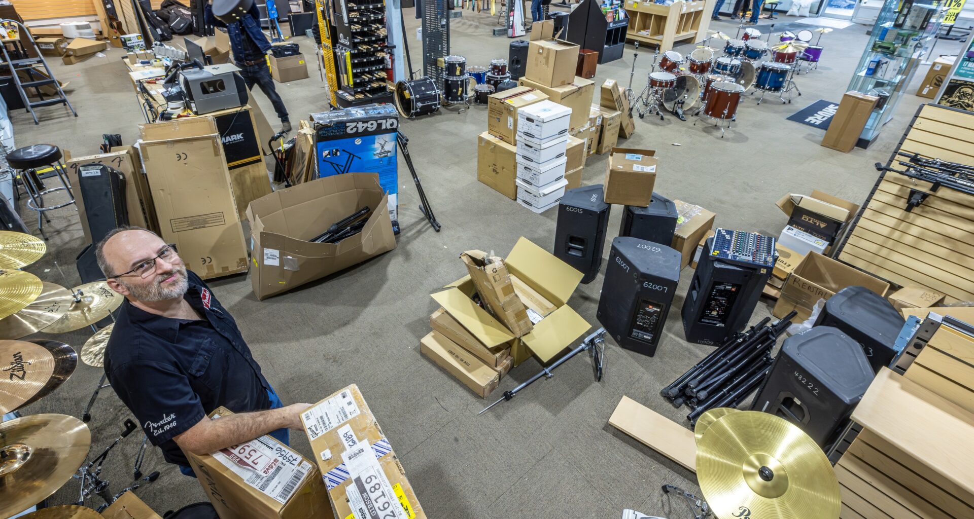 Man stands amid boxes of musical instruments in store.
