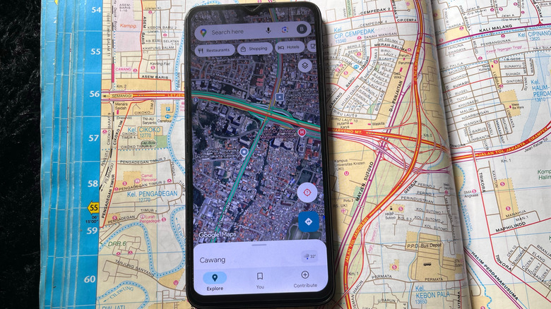 A smartphone running the Google Maps app on top of a paper map.