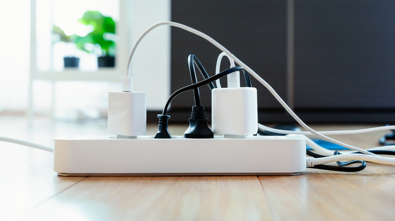 A white power strip on a wooden floor with power adapters attached to it.