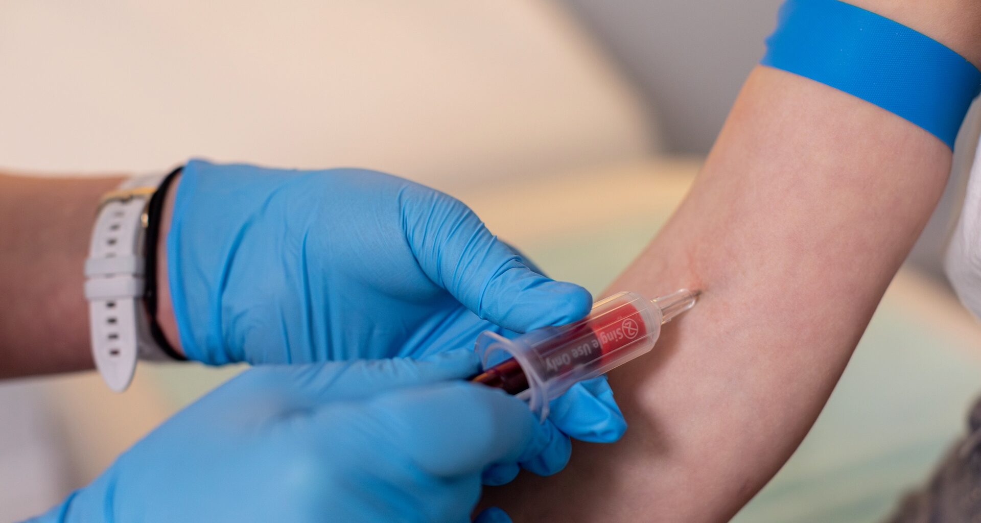 A healthcare professional draws blood from a patient's arm while wearing blue gloves.