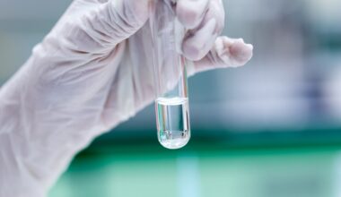 A gloved hand holds a test tube containing a clear liquid against a blurred laboratory background.