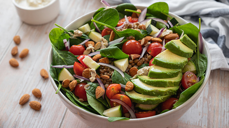 Fresh salad in a bowl, topped with avocados, almonds, onions, and cherry tomatoes