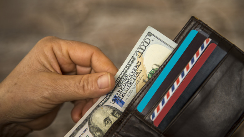 hand holding wallet pulling out a hundred dollar bill