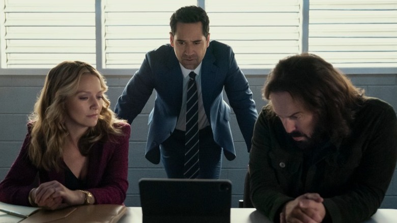 Mickey Haller standing over Lorna and Cisco as they look at a tablet in The Lincoln Lawyer Season 4