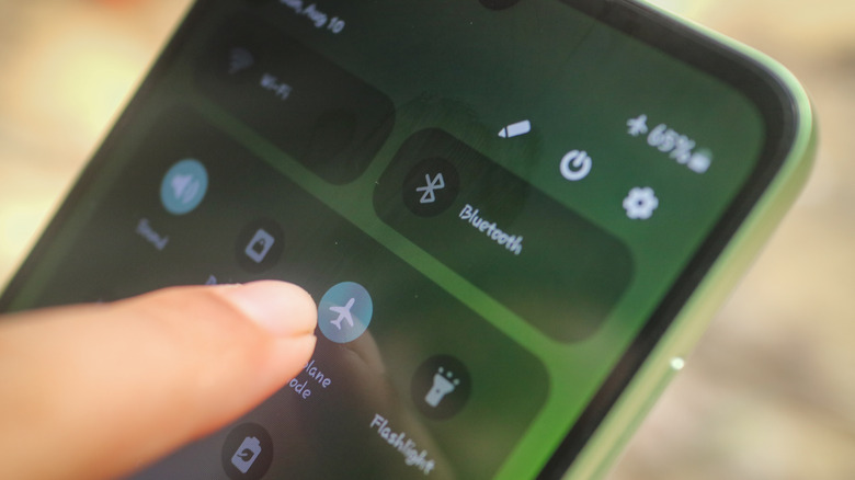 A finger touching the airplane mode icon on a phone.