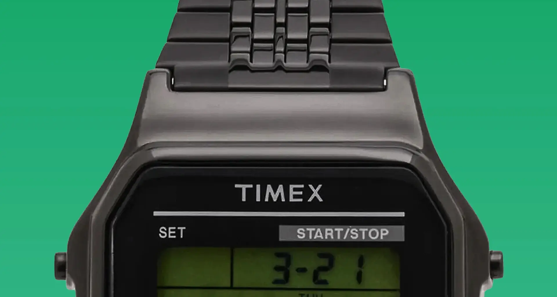 Close-up of a black Timex digital watch face with metal link band on a green background.