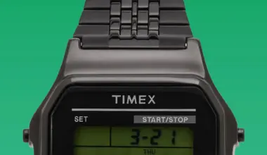 Close-up of a black Timex digital watch face with metal link band on a green background.