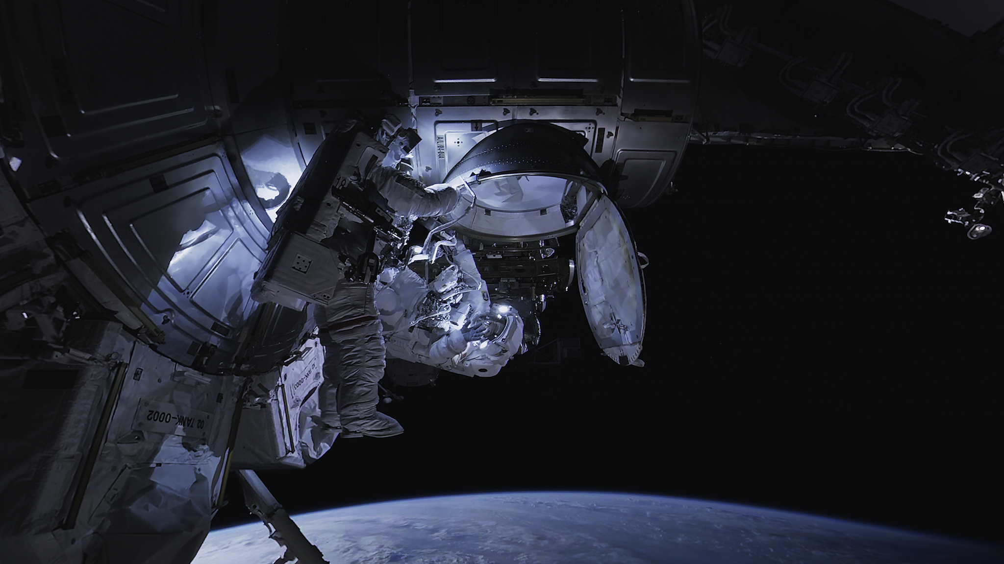 A photo of spacewalkers outside the ISS. The Earth is below.