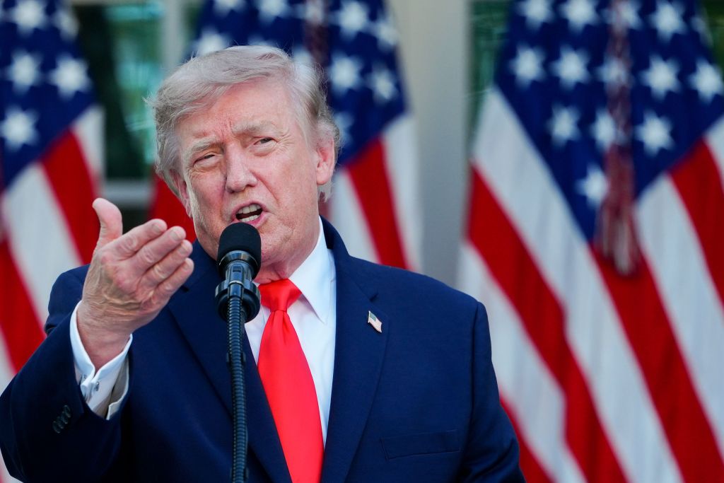 Donald Trump speaking at a microphone with American flags behind him.