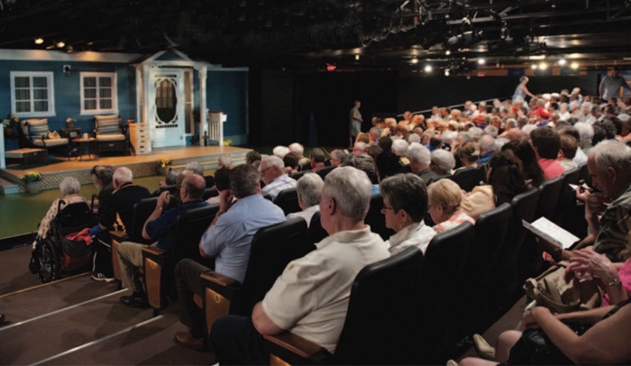 audience in a small theatre looking toward a stage set of a house