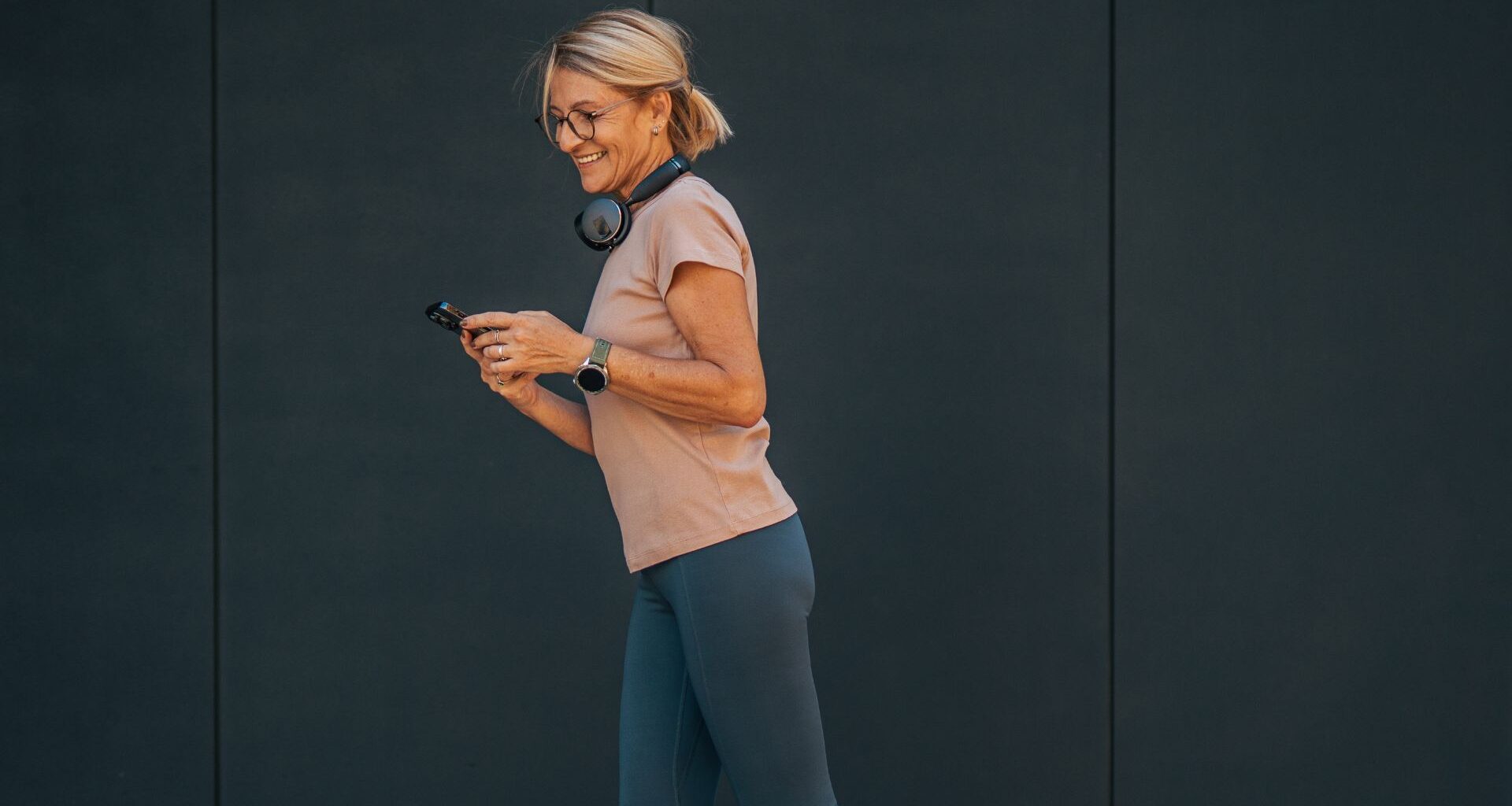 Woman walking wearing fitness tracker, smiling and looking at phone to check step count