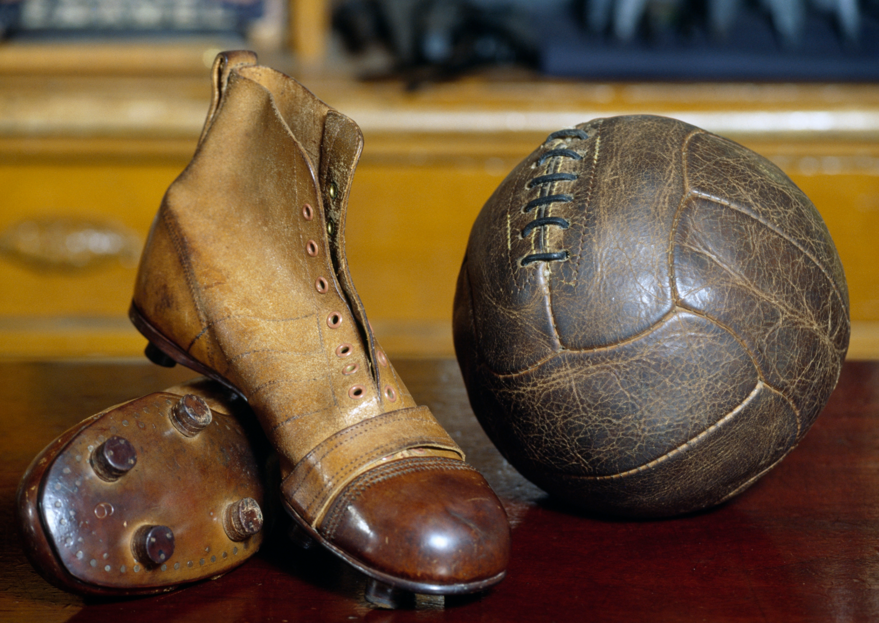 a vintage soccer ball and cleats in a museum. they are both made of brown leather