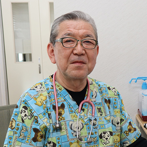 An Asian man wearing blue and green scrubs and glasses looks at the camera.