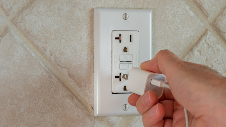 A hand plugging a power block with a cable into the wall.