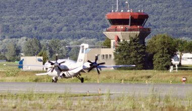 A small aircraft taxis down the runway past the control tower.