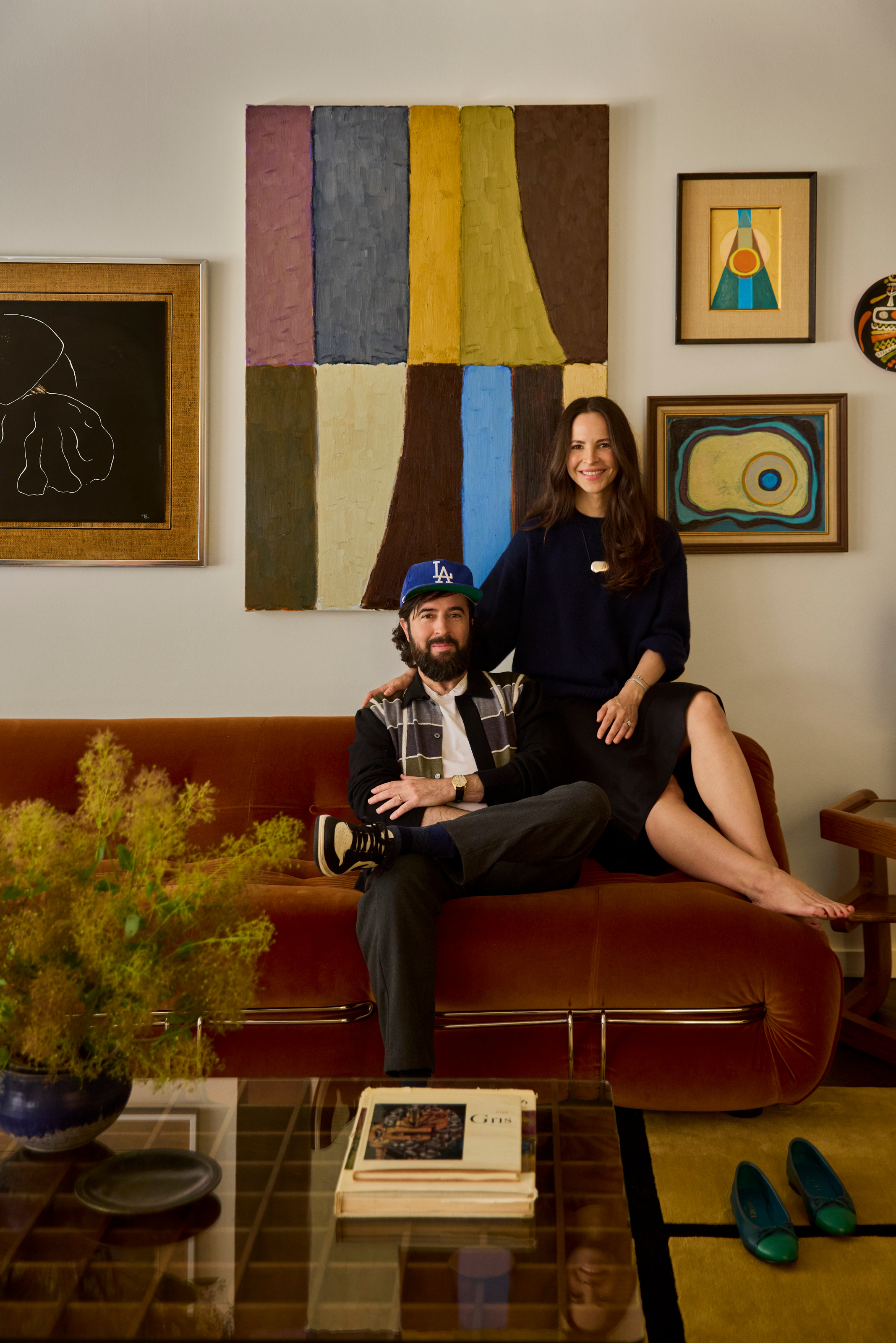 Owners Chloe and Jeremy sitting on a rust-colored velvet sofa in front of a gallery wall