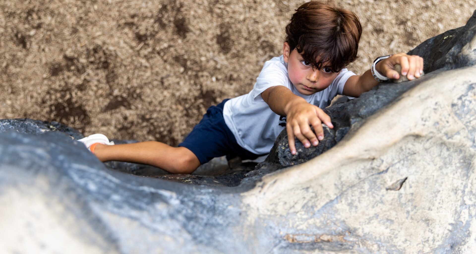 Seen from above, a boy looks determined as he climbs a rock wall.