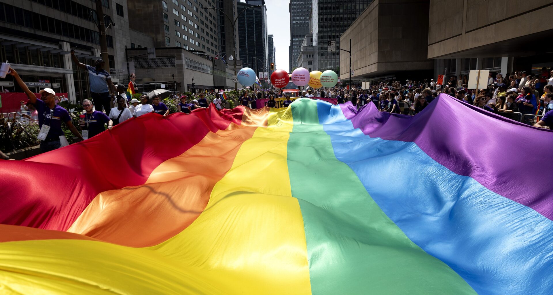 Participants in the 2026 Montreal Pride parade carry a large rainbow banner down Réné-Lévesque Boulevard