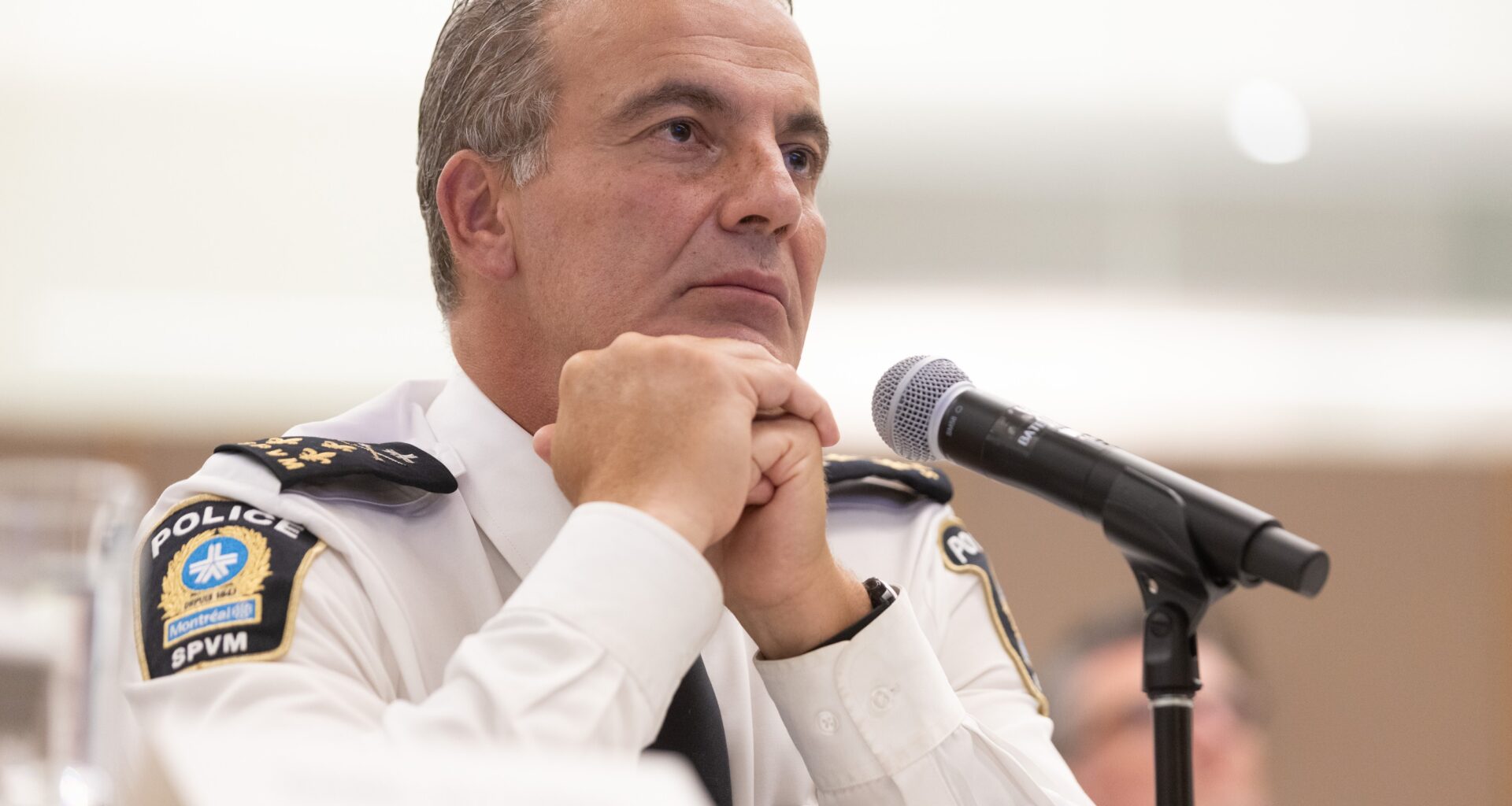 Montreal Police Chief Fady Dagher sits behind a microphone with his hands folded as he listens to a question from a citizen at a public hearing.