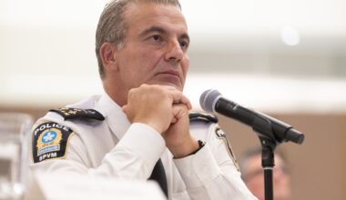 Montreal Police Chief Fady Dagher sits behind a microphone with his hands folded as he listens to a question from a citizen at a public hearing.