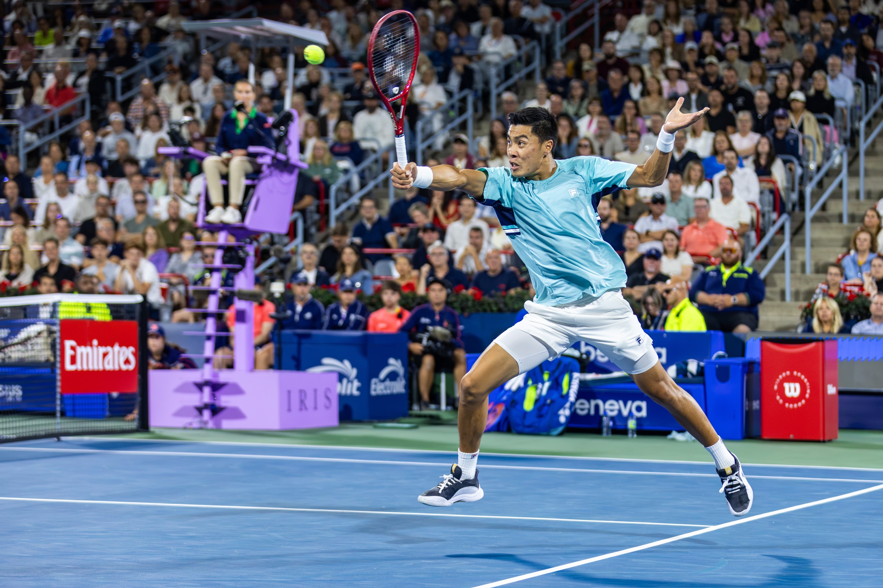Brandon Nakashima's feet are off the ground as he hits a tennis ball.