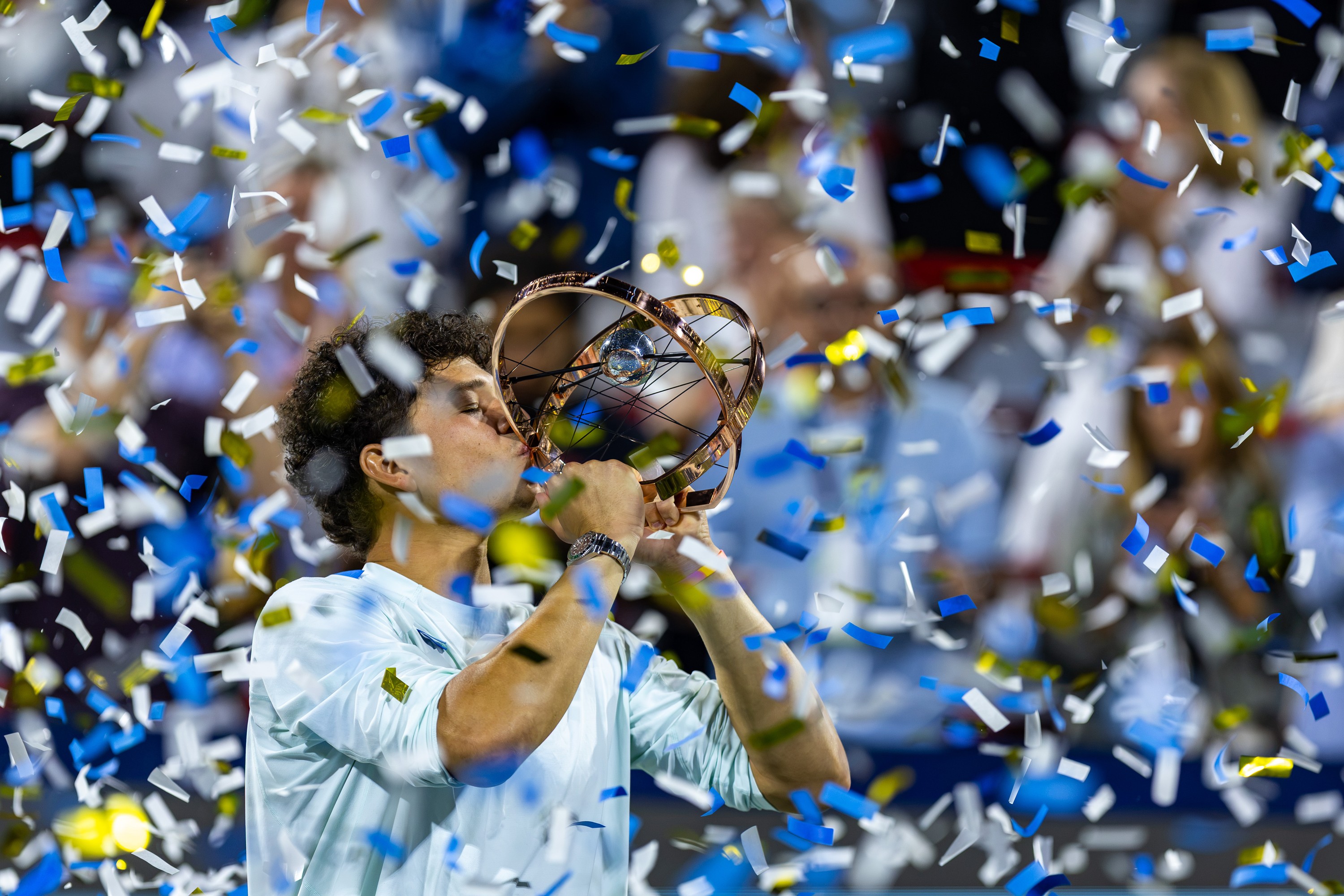 Ben Shelton, obscured by confetti, kisses his trophy.