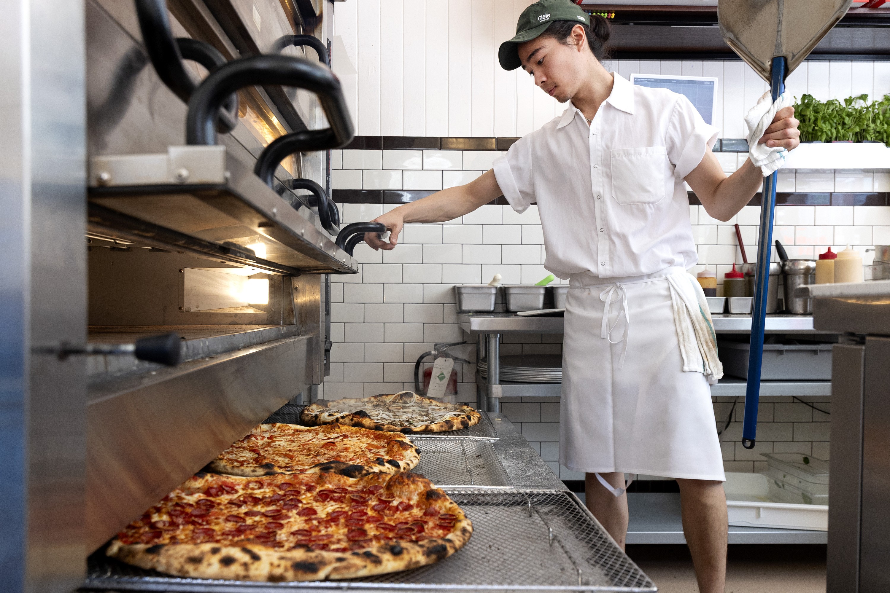 A pizzaiolo at Pizzeria Elena surveys three pizzas that have just been pulled from the oven.