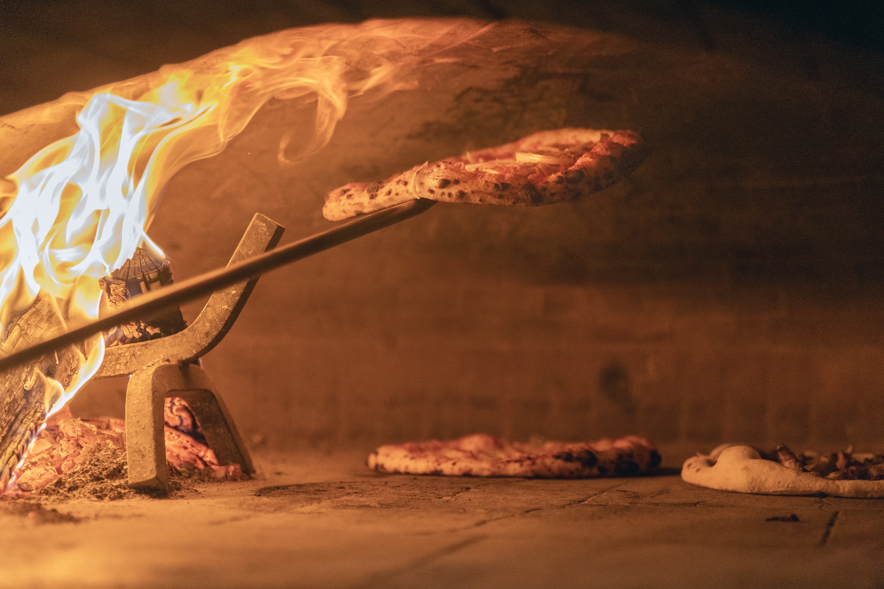 Elena's pizza oven glows with wood-fired flame and two pizza baking.