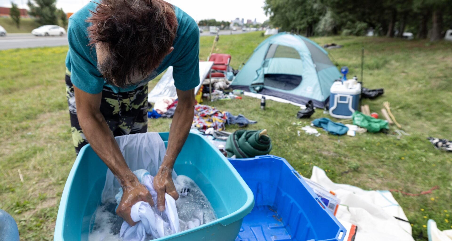 Man washes clothes in a basin outside a tent.