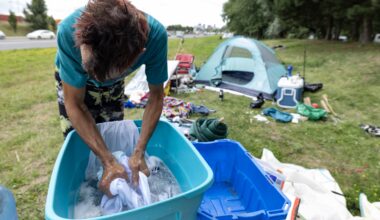 Man washes clothes in a basin outside a tent.