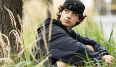 Jacob Whiteduck-Lavoie sitting in the grass near a tree, wearing a backwards ball cap.