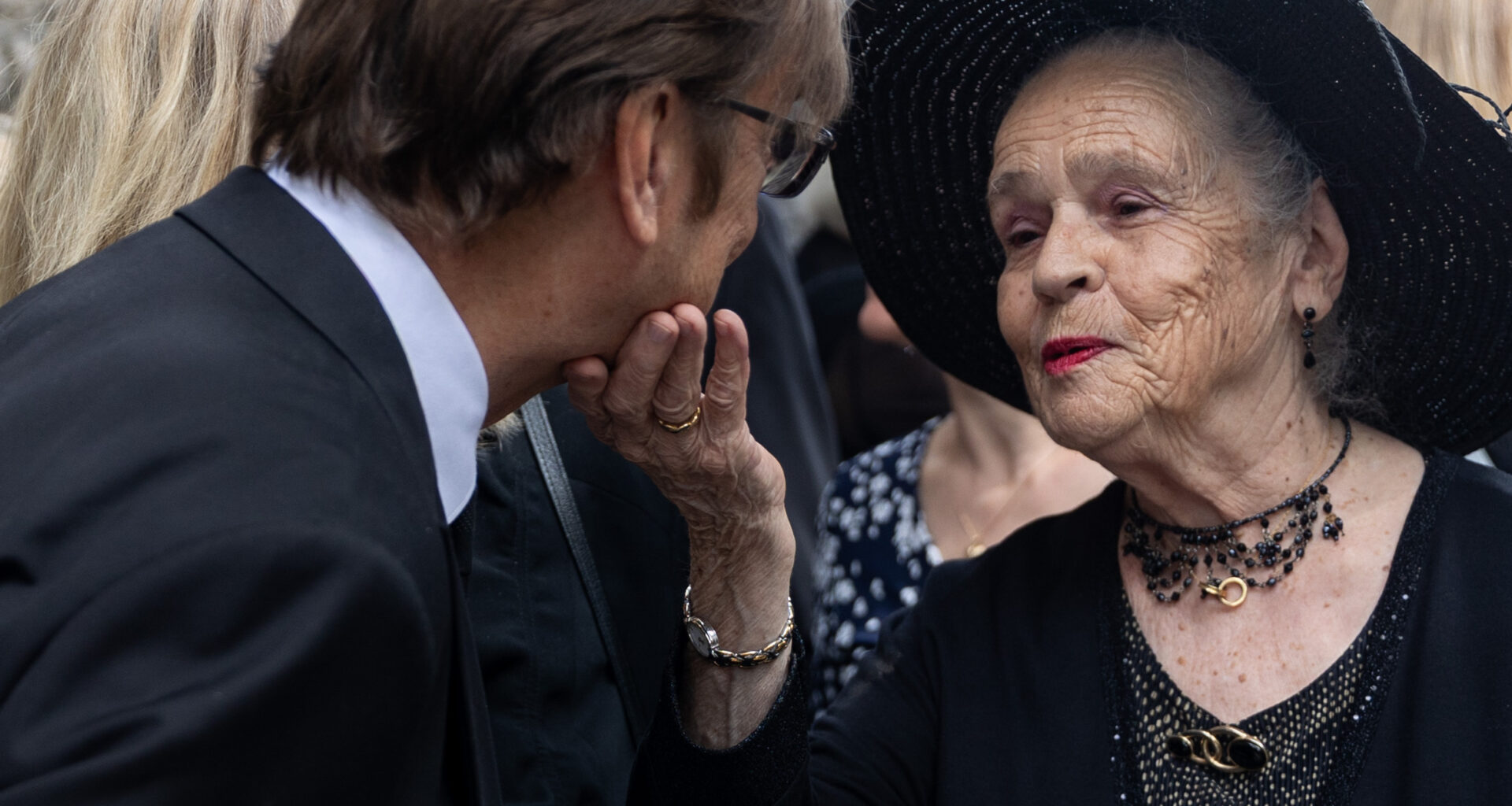 A widow touches the chin of a mourner at a funeral.