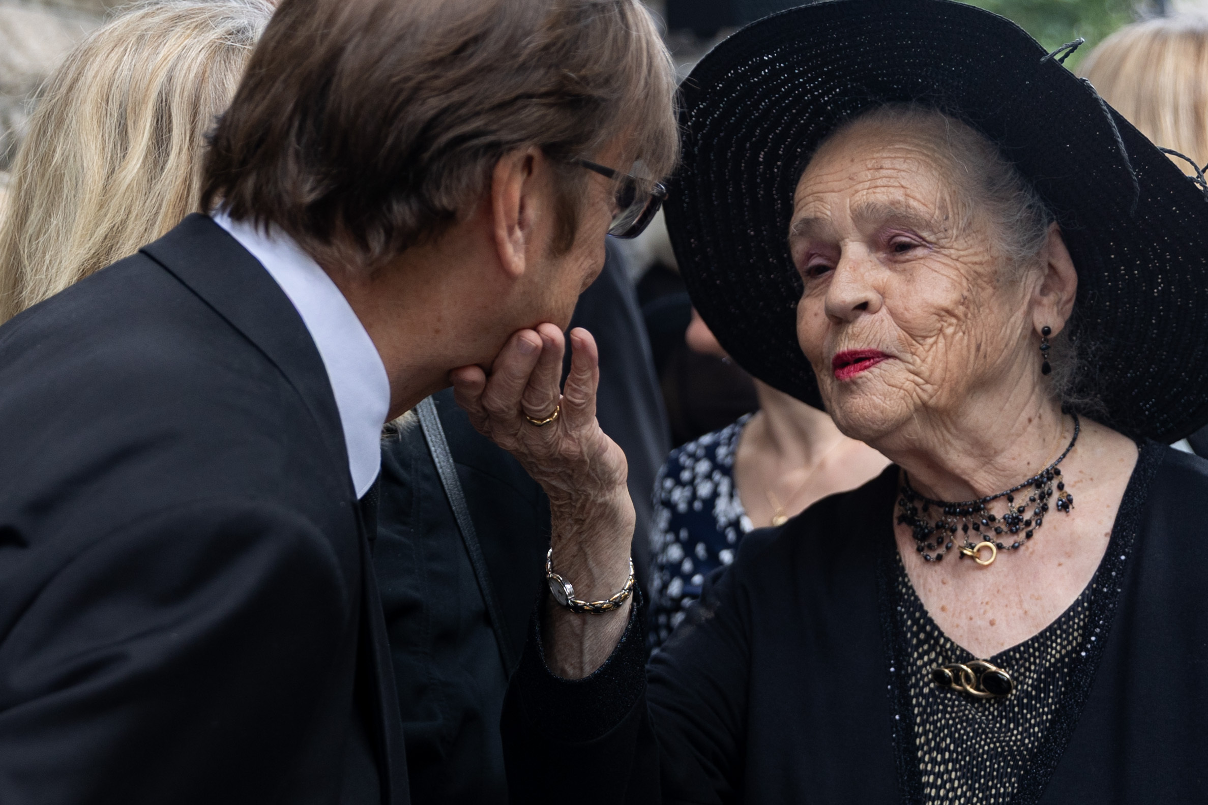 A widow touches the chin of a mourner at a funeral.