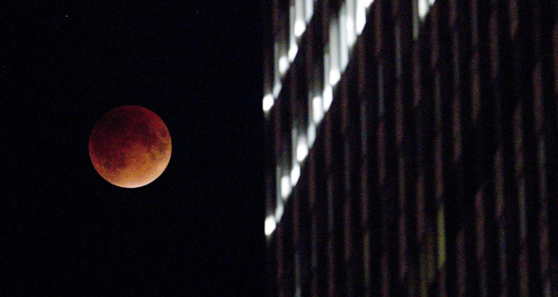A reddish, eclipsed moon next to an office building.