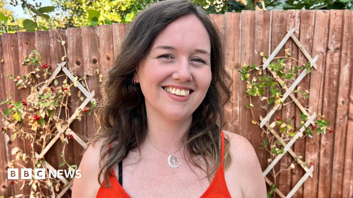 A white woman with brown hair smiles in the garden looking at the camera.