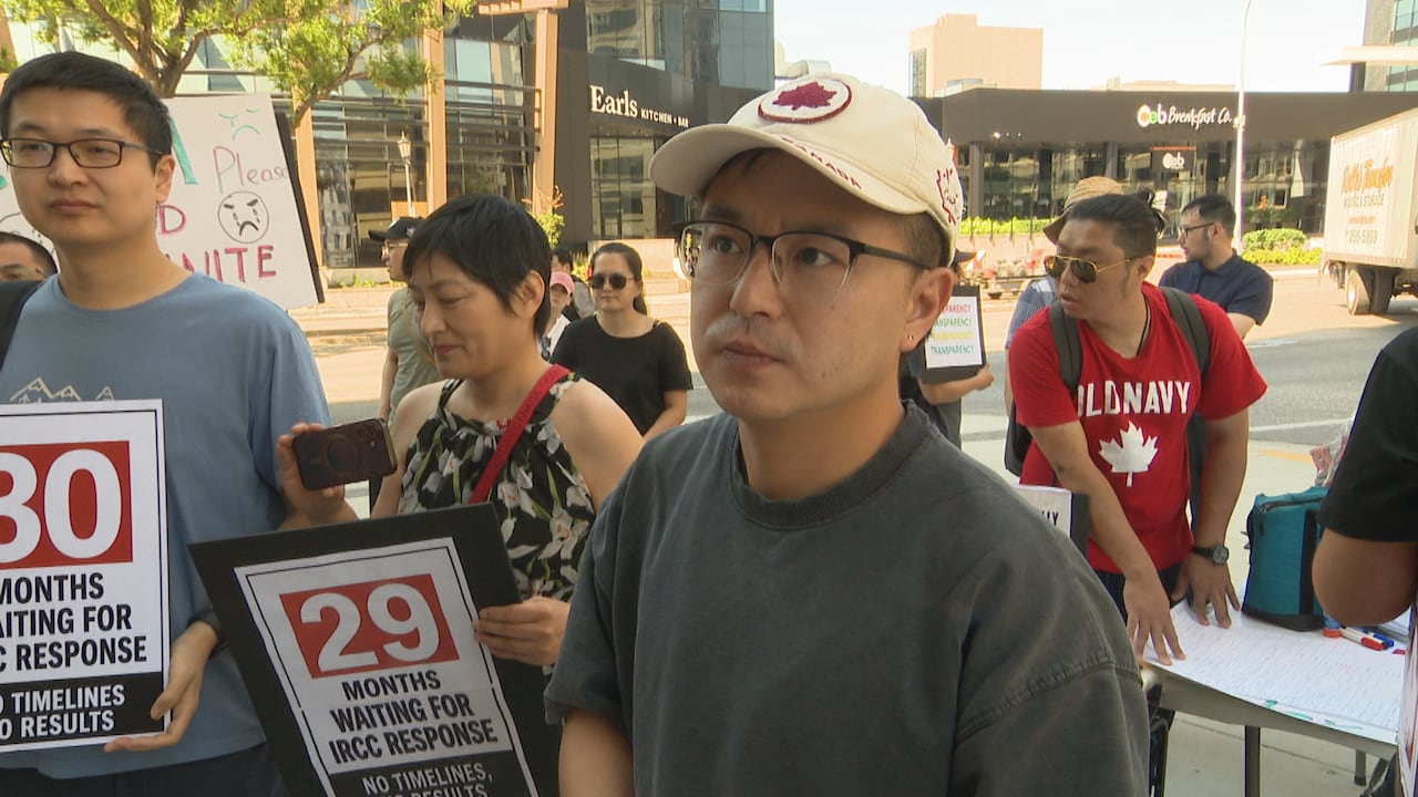 A man wearing a white and red hat with a Canadian maple leaf stands among a crowd on a city street