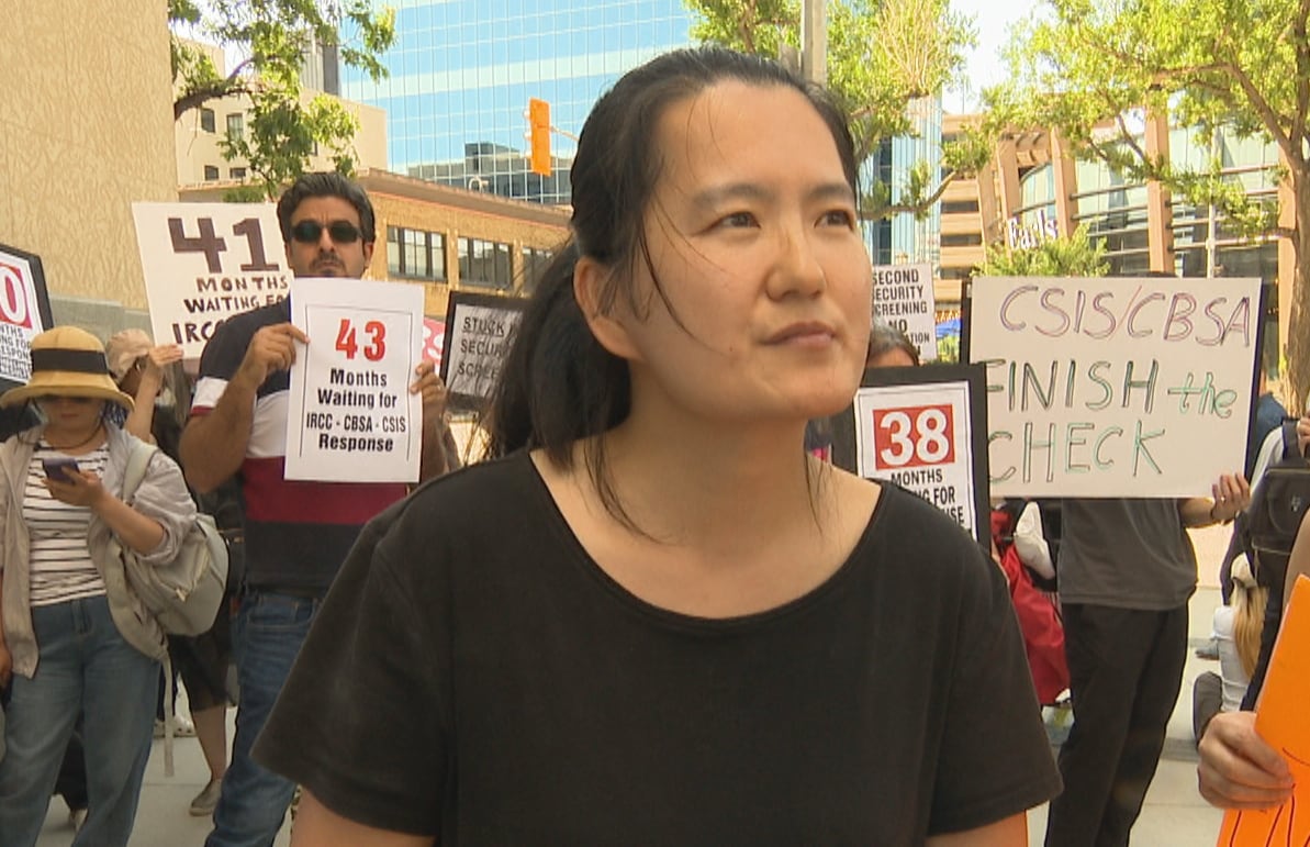 A woman with dark hair pulled back into a ponytail wears a black shirt and stands in a crowd of people holding signs.