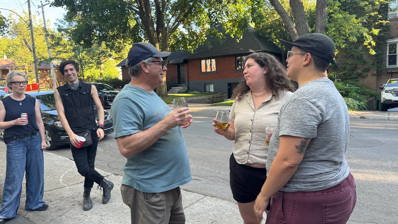 Five people stand on a sidewalk chatting.