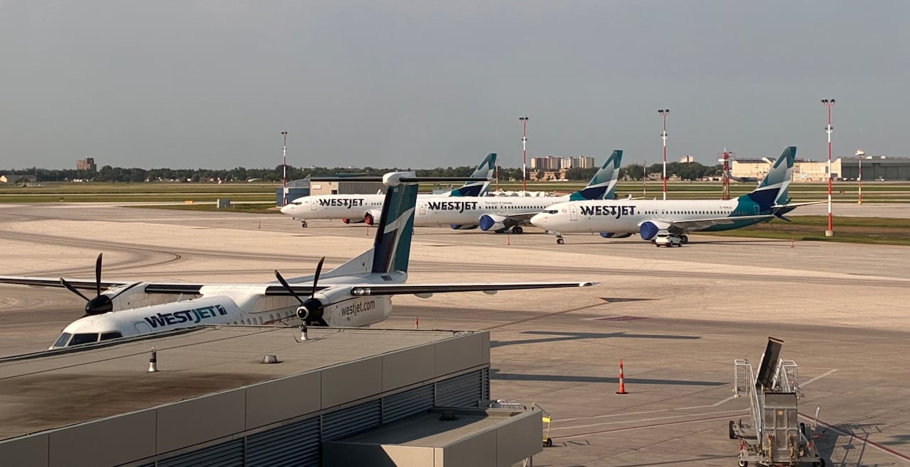 A group of white and blue planes with "WestJet" branding are parked on a tarmac at an airport