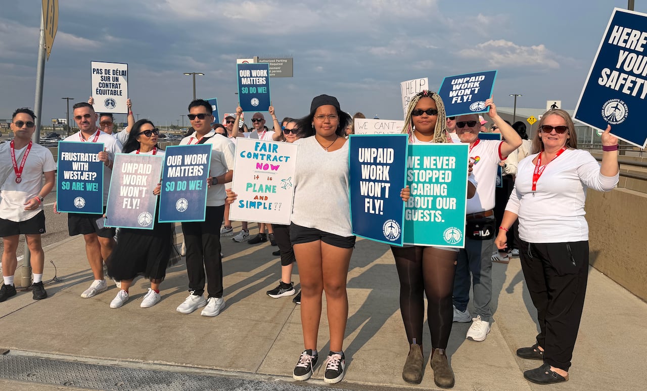 People holding signs that reads 'Unpaid work won't fly!' and 'Our work matters. So do we!' among other messages stand outdoors.