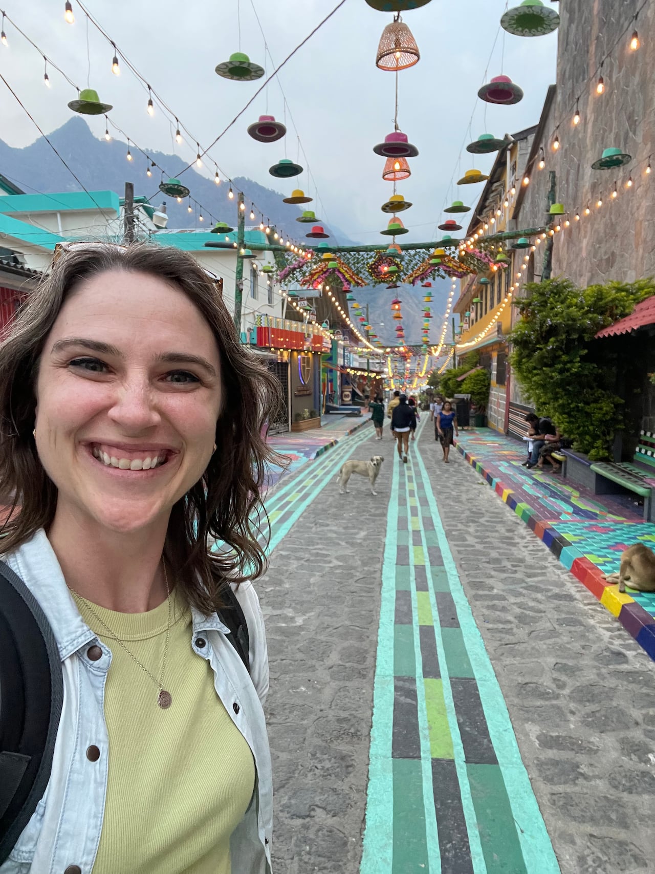 A woman is smiling and a colourful street with hanging lamps are behind her.