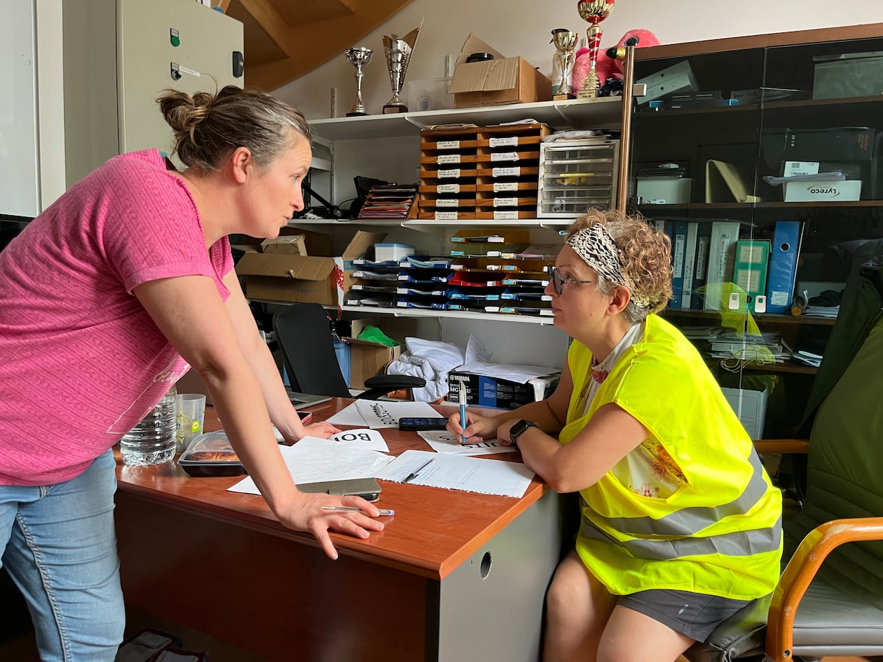 Two women speak at a desk in an office.