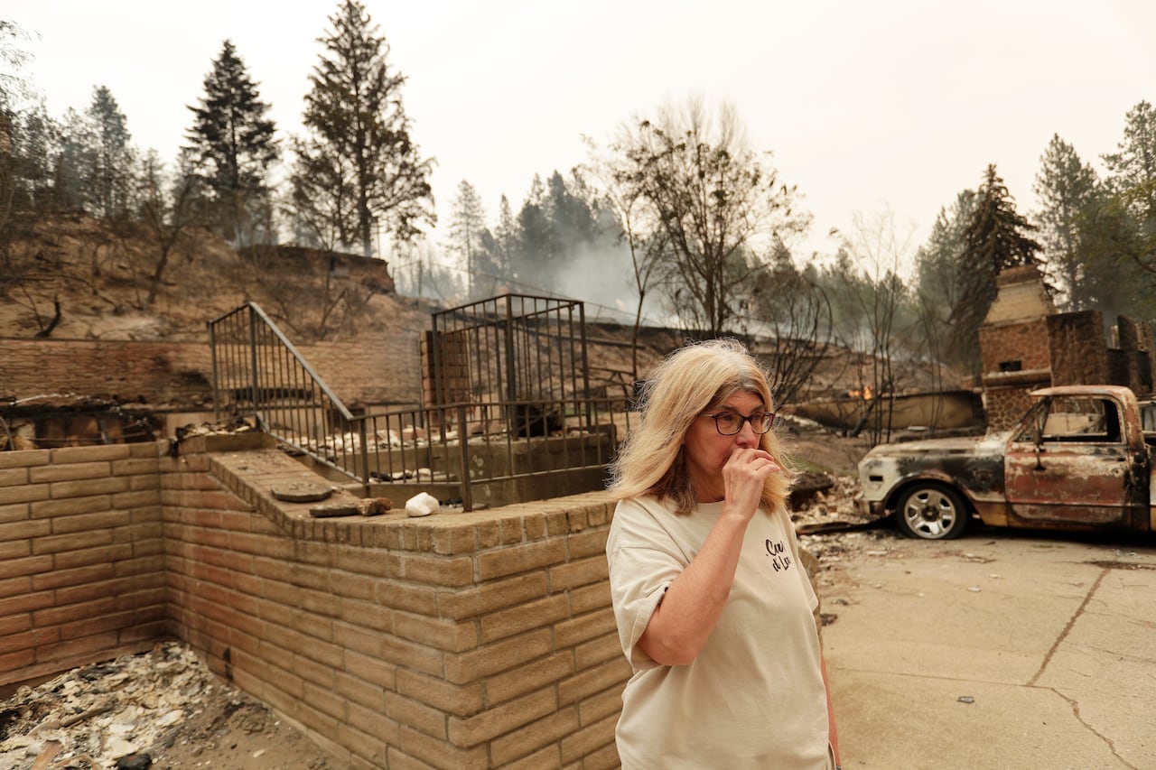 A person stands near a destroyed home and vehicle.