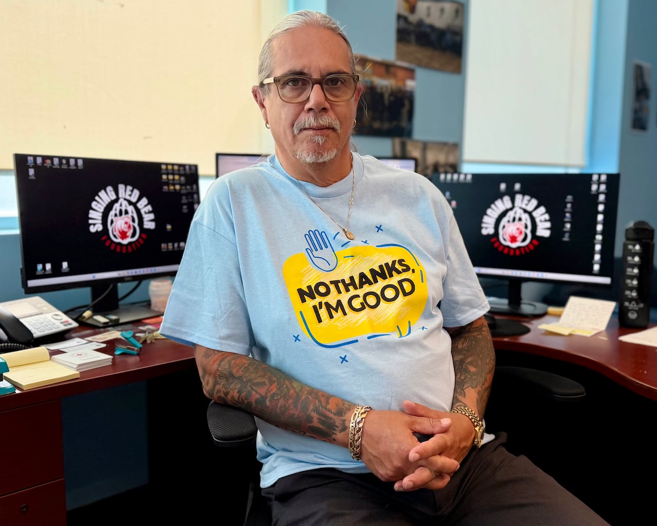 A man in a blue and yellow shirt poses for a picture by a computer