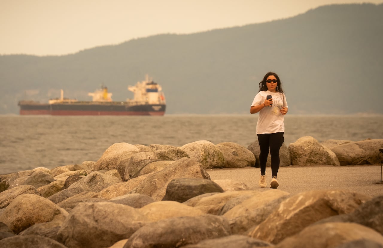 A woman jogs along a seaside path with visibly orange skies around her. A ship is in the background.