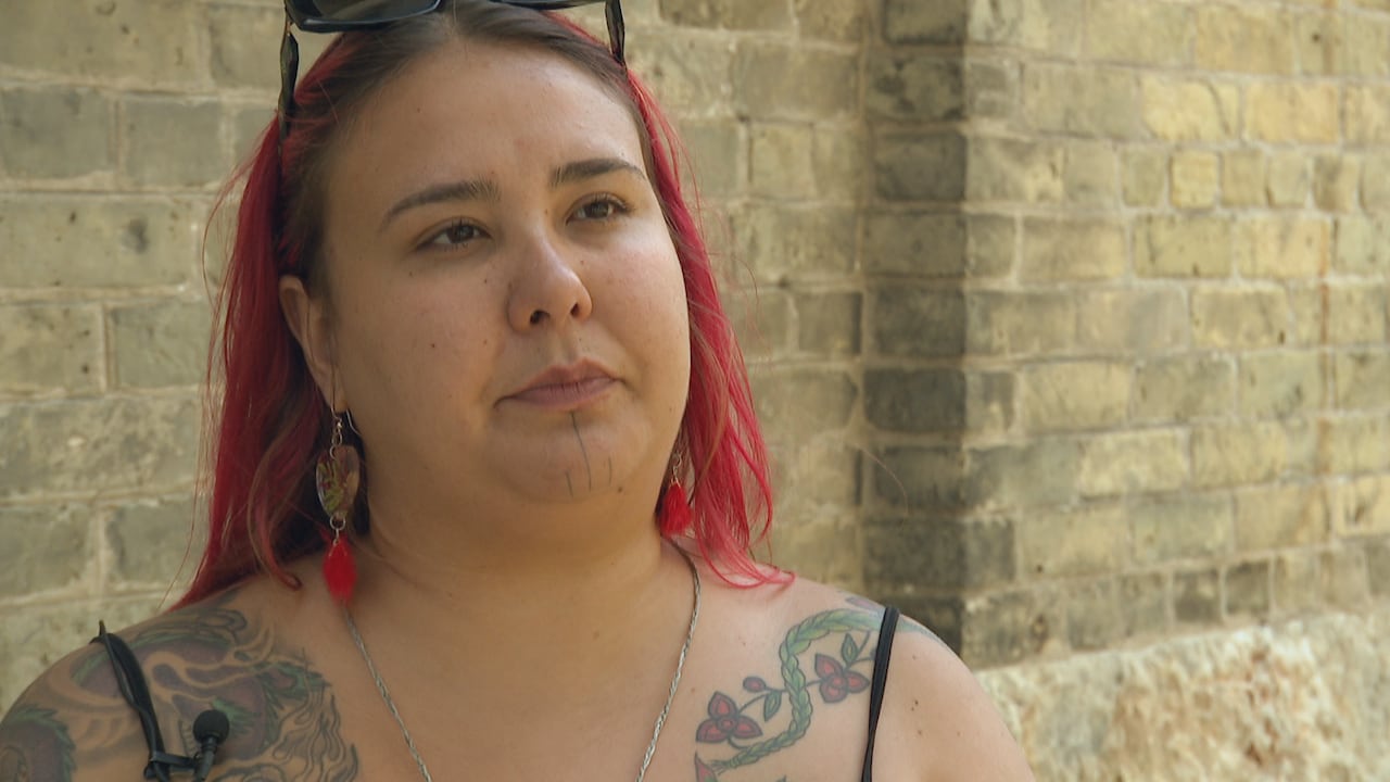 A woman with pink hair stands in front of a brick building.