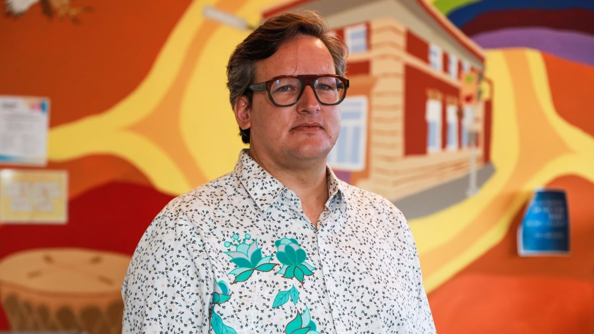 A man with glasses looks at the camera.