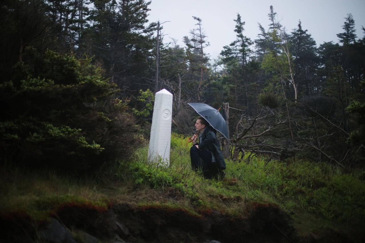 A man with an umbrella kneeling in front of a white cenopath. They are surrounded by woods.